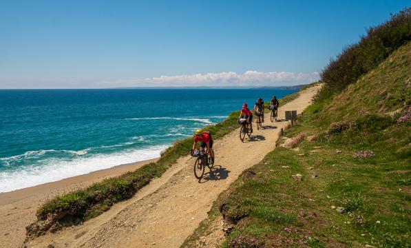 Four people cycling downhill on an off road route with hills to their left and the sea to their right on a sunny day