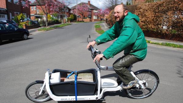 A man in a green puffa jacket and green trousers is riding a white e-cargo bike carrying 110kg of concrete