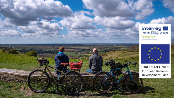 Two men sit on a bench looking out at a view of rolling hills