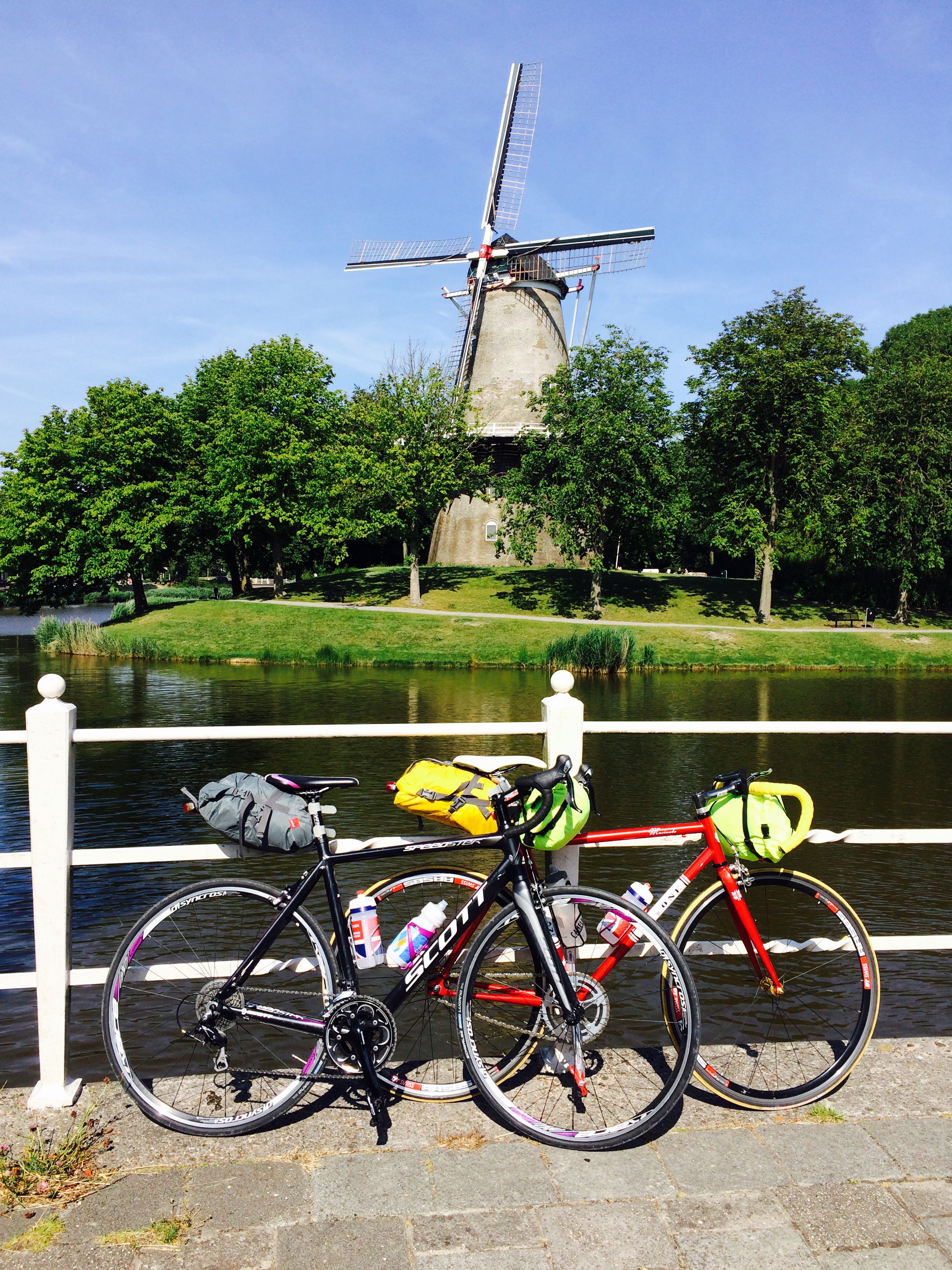 Two bikes leaning up against a fence with a canal behind it and a windmill in the distance