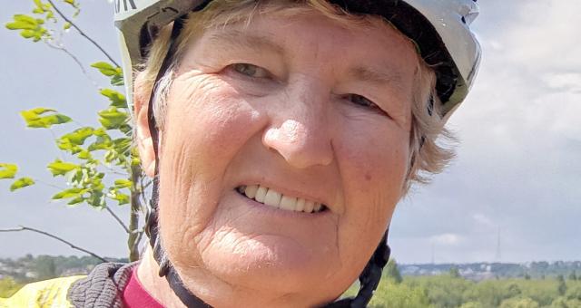 A selfie of Ann Ferris. She is wearing a yellow waterproof cycling jacket with a pink jersey underneath. She has a white cycling helmet.