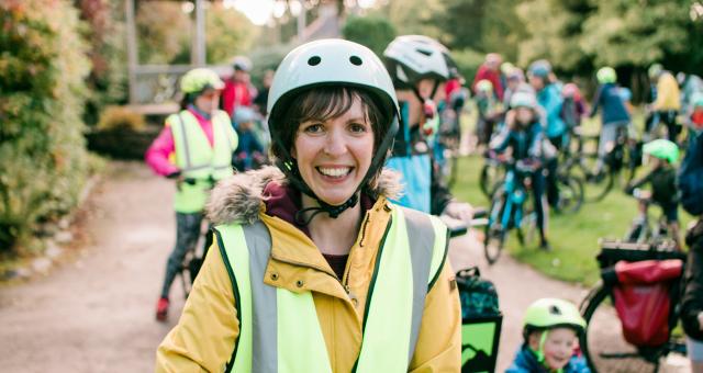 Bridie Barnett is smiling at the camera. She is wearing a white cycle helmet, a yellow jacket and yellow hi-vis vest. She is at a cycling event with loads of adults and kids with their bikes in the background.  Photo: Katie Noble