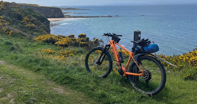 Orange ebike leaning against a pole on an offroad track with a view of the ocean behind it