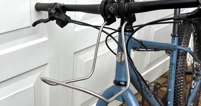 A close-up shot showing the Bagman Universal Bar Rack attached to the handlebar of a blue Genesis mountain bike