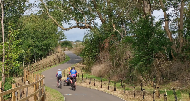 Two cyclists in the distance on a cycle path surrounded by green trees