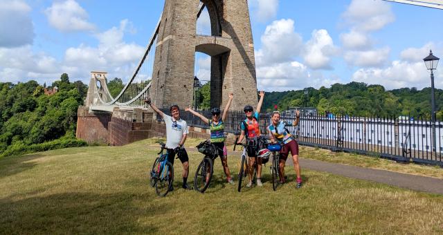 Four cyclists standing with their bikes next to the a bridge on their way to Glastonbury