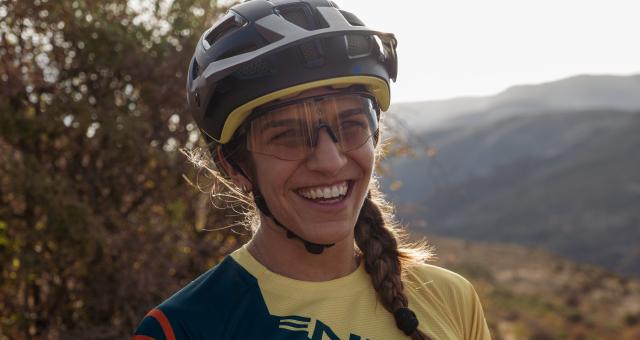 Jasmin Patel is pictured smiling wearing a cycle helmet and glasses with a mountain range and trees in the background