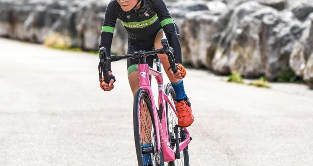 Olivia Smallshaw racing her pink road bike in Shibden CC cycling kit. She is wearing a pink helmet and cycling sunglasses. She looks like she’s concentrating hard.