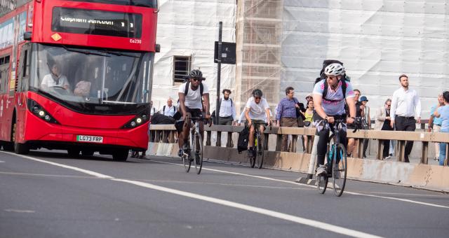 Two cyclists on a cycle and bus lane on London Bridge with a bus behind them