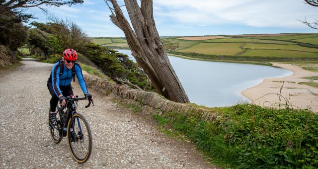 Man cycling in Cornwall on a gravel track with a lake to his left