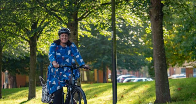 Victoria Hazael rides a Raleigh Motus bike along a quiet tree-lined street. She is wearing a blue dress and cycle helmet