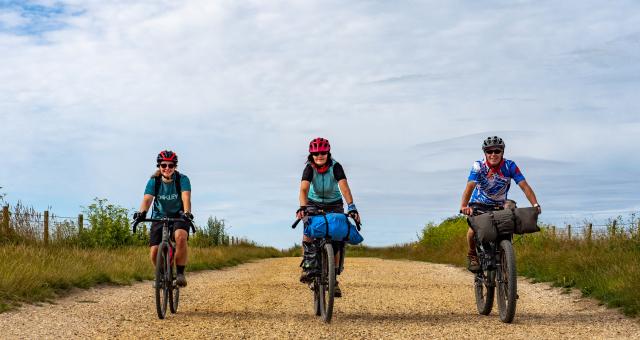 Three cyclists in a row, riding towards the camera on a gravel track