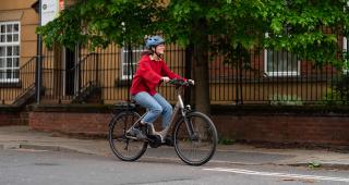 Woman in a red jumper cycling an ebike on the road (c) JoeCotterill/CyclingUK