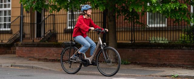 Woman in a red jumper cycling an ebike on the road (c) JoeCotterill/CyclingUK