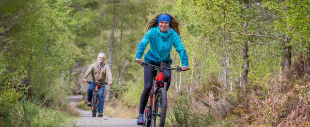 Women off road cycling in the sun on a gravel path, with a man cycling behind