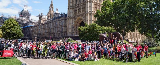 A large group of women on bikes standing outside the houses of Parliament at the Womens Festival of Cycling event