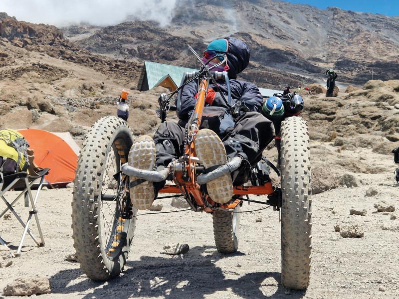 A woman in on a mountain trike at a mountain campsite. Tents can be seen in the background