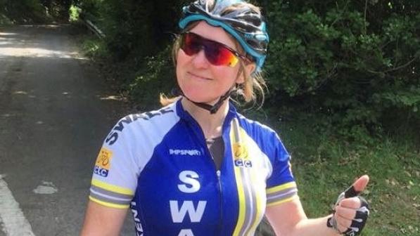 A woman in cycling clothing is smiling and putting her thumb up