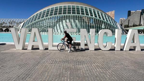 A man on a road bike is posing in front of the Valencia sign with the Hemisferic planetarium behind