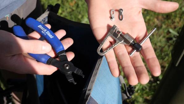 A person is holding some bicycle repair kit: a pair of pliers, a chain breaker tool and a quick link