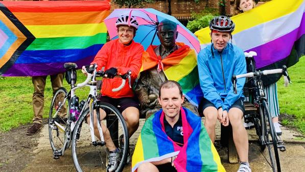 A group of people is posing with rainbow flags and their bikes