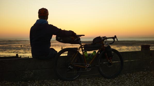 Someone sat down next to their bike over looking the sea while the sun sets