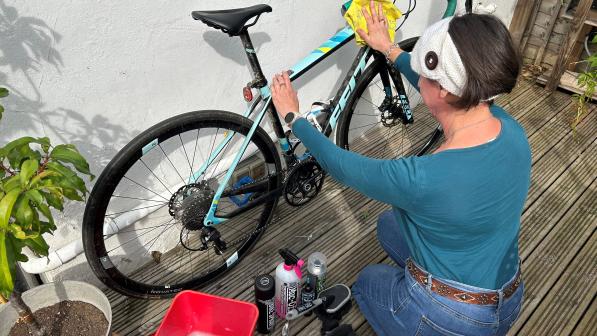 A woman is cleaning a Felt road bike that's leaning up against a white wall. There's a bucket of soapy water and loads of cleaning products next to her
