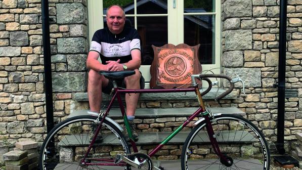 A man sits on a window sill behind his vintage bicycle. A winged-wheel CTC plaque is beside him