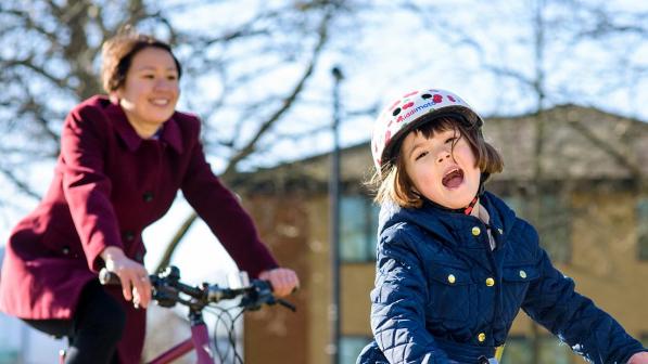 A child cycling to school with her mother