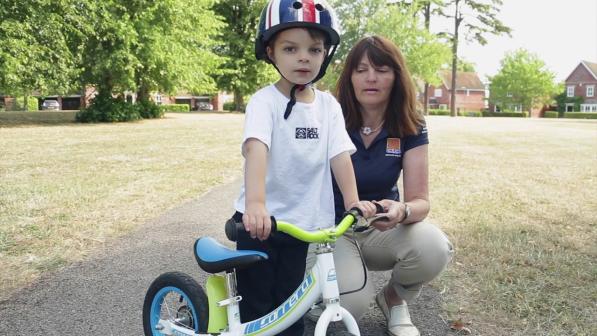 A child being taught how to ride a balance bike.